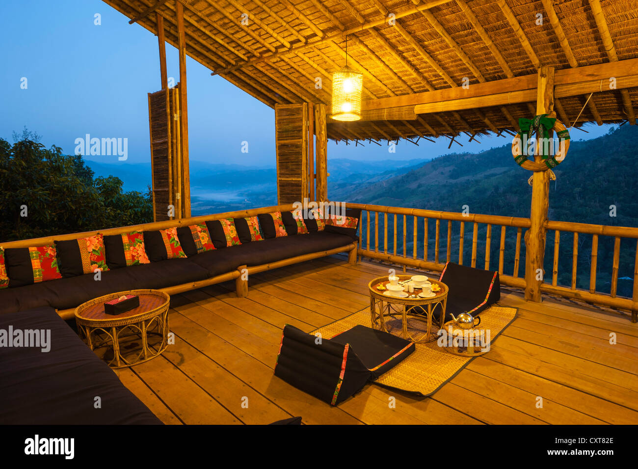 Set de table pour deux avec coussins d'assise sur un porche ou une véranda au crépuscule, bamboo hut, Lanjia Lodge, dans le Nord de la Thaïlande, la Thaïlande, l'Asie Banque D'Images