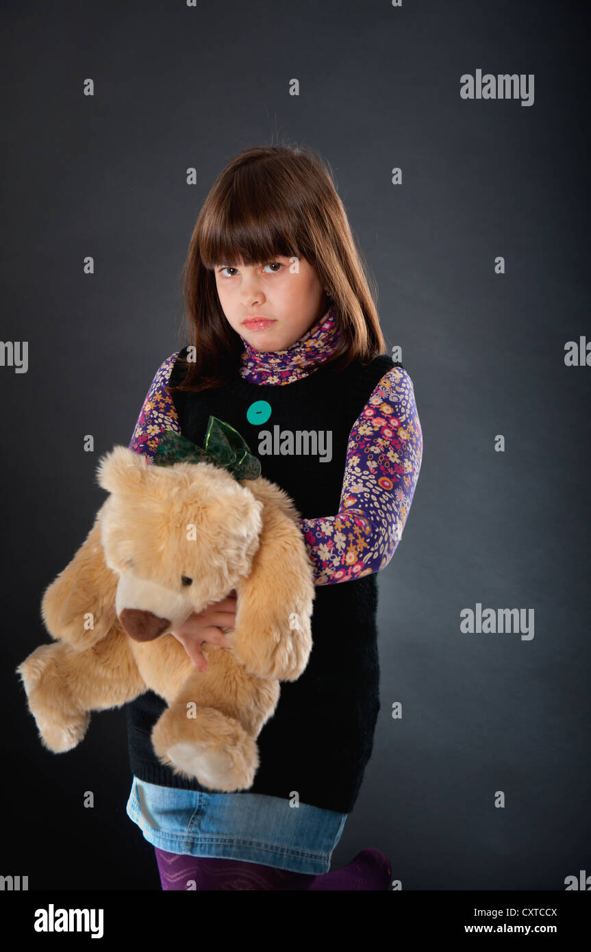 Jolie fille triste en fond sombre jouant avec son ours en peluche Banque D'Images