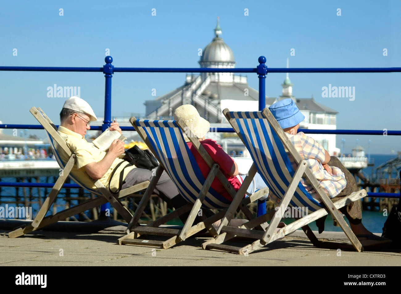 Plusieurs personnes âgées de portrait horizontal des gens assis sur des chaises longues en profitant de la vue de la jetée et de mer sur un jour ensoleillé Banque D'Images