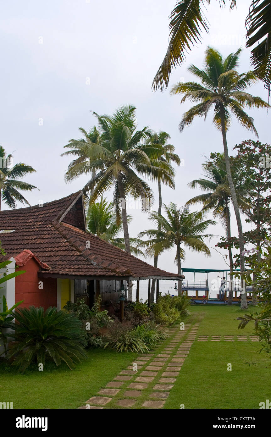 Vue verticale de teck en bois bungalows dans un resort dans les Backwaters du Kerala, avec un bateau d'excursion en attente de clients. Banque D'Images