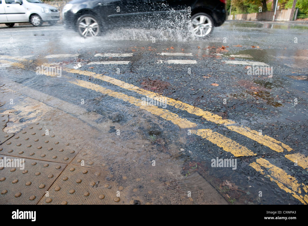 L'eau des inondations en rafale de la canalisation principale route avec des voitures passant devant Banque D'Images