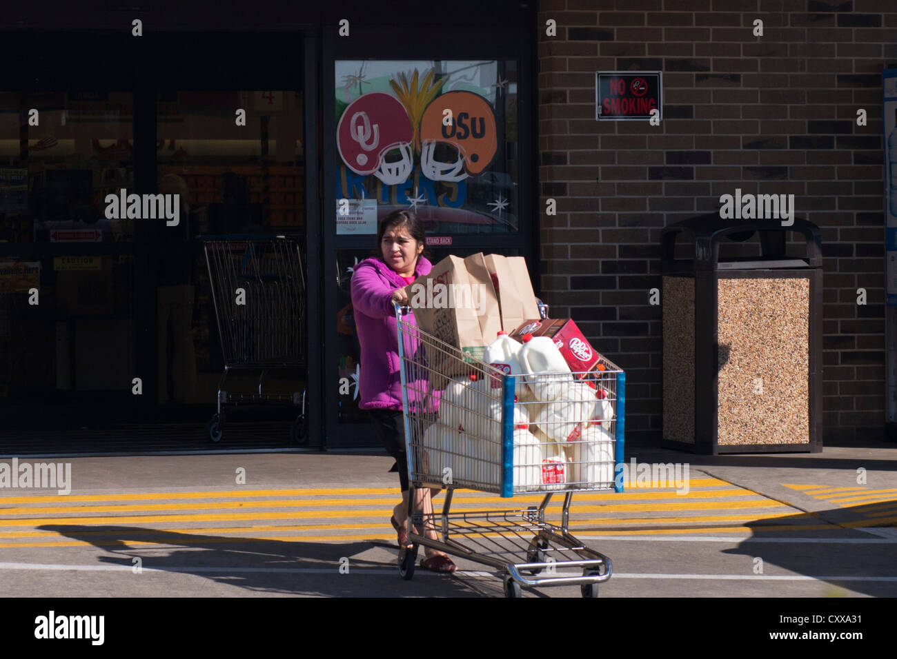 Une jeune femme hispanique de l'embonpoint pousse un panier chargé avec du lait et les sacs d'un supermarché à New York, USA. Banque D'Images
