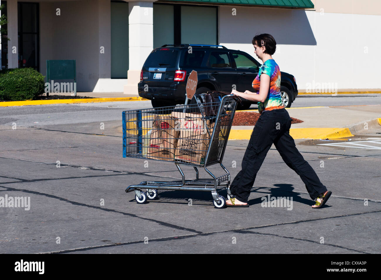 Une jeune femme de race blanche pousse un panier avec de la nourriture licenciés dans une aire de stationnement. Oklahoma City, Oklahoma, USA. Banque D'Images