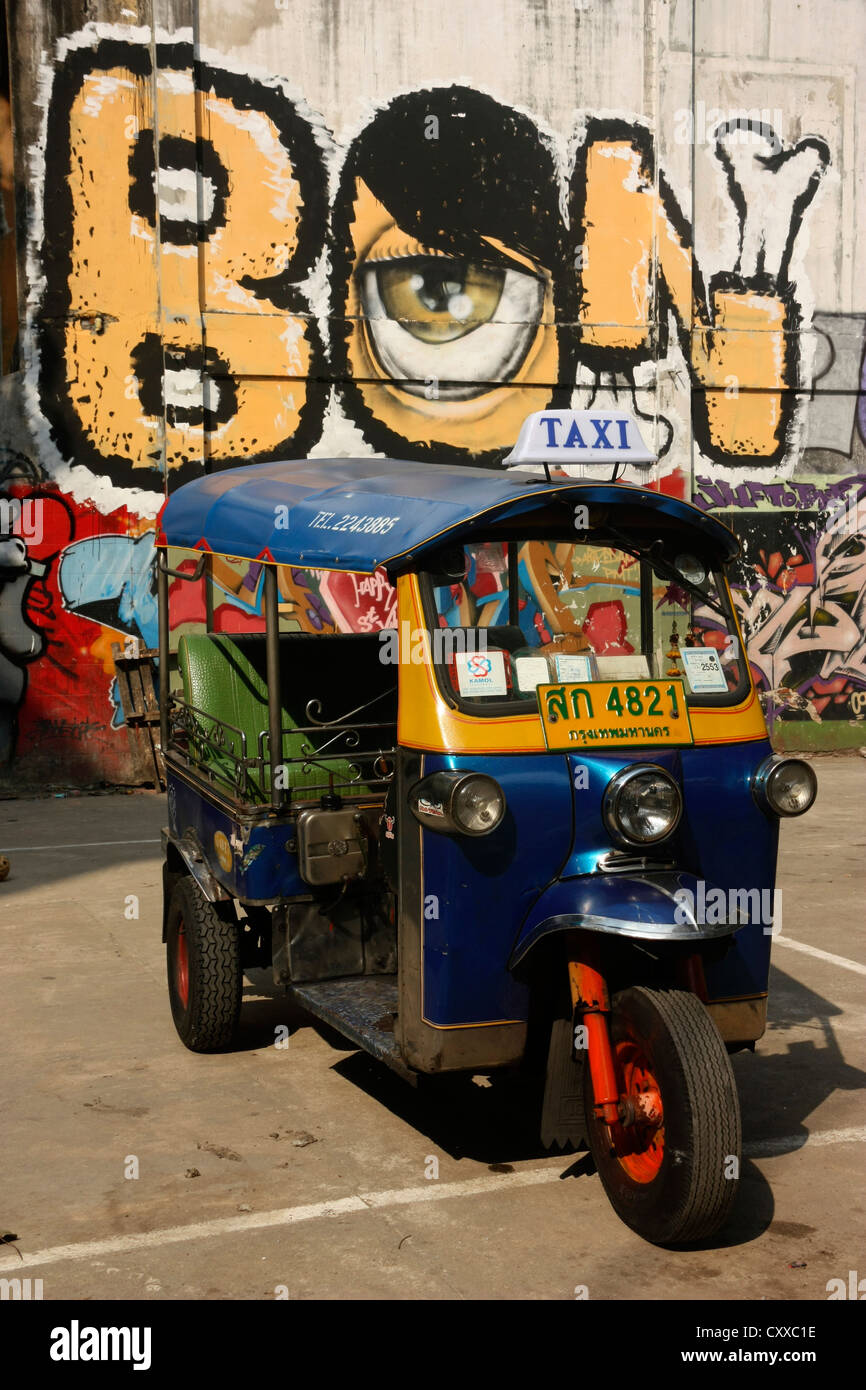 Moteur Tricycle taxi pousse-pousse en avant du mur de graffiti Bangkok, Thaïlande Banque D'Images