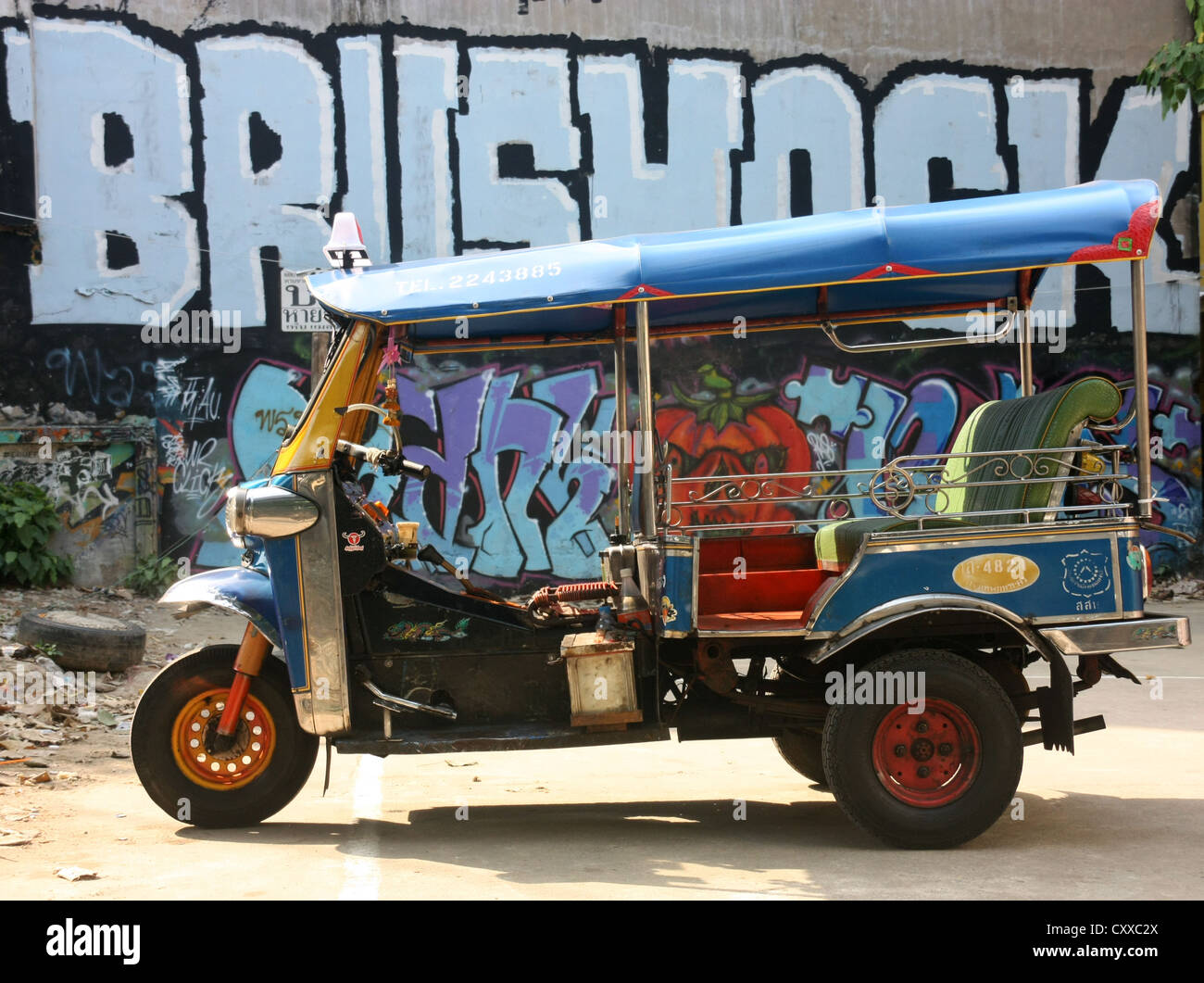 Moteur Tricycle taxi pousse-pousse en avant du mur de graffiti Bangkok, Thaïlande Banque D'Images