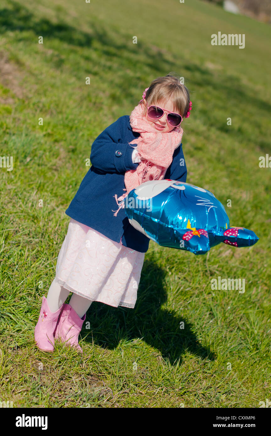 Une fille de congélation avec lunettes roses à l'extérieur avec un ballon-lapin bleu Banque D'Images