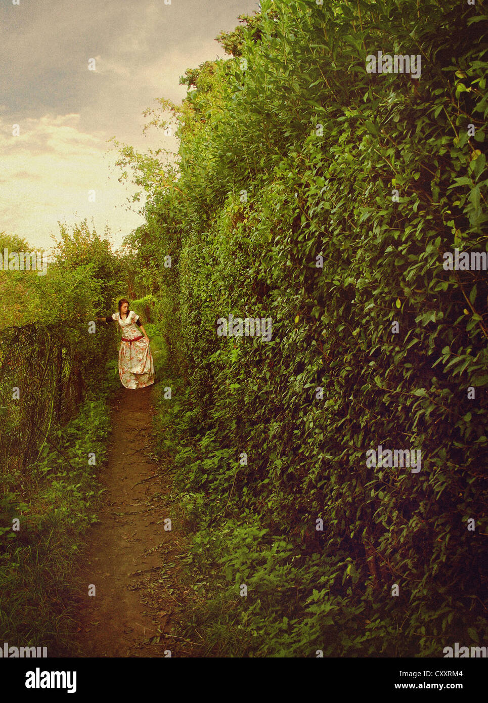 Une femme en robe blanche, marcher le long d'un chemin dans un jardin / labyrinthe. Banque D'Images