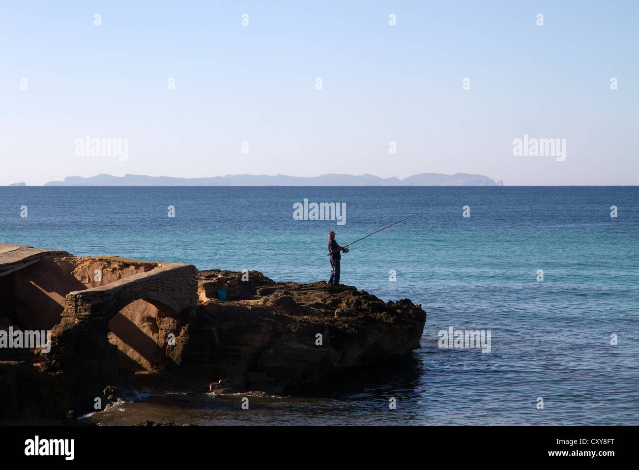 L'homme pêche en mer Méditerranée par l'eau de roche, l'île de Cabrera sur fond d'horizon, Majorque Îles Baléares Espagne Banque D'Images