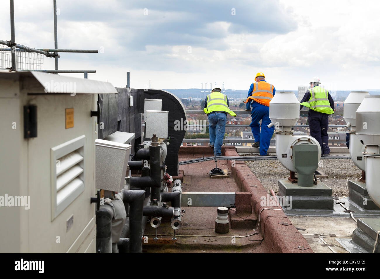 Trois ouvriers vestes haute visibilité et un casque sur le toit de l'usine de traitement de l'air entre Banque D'Images