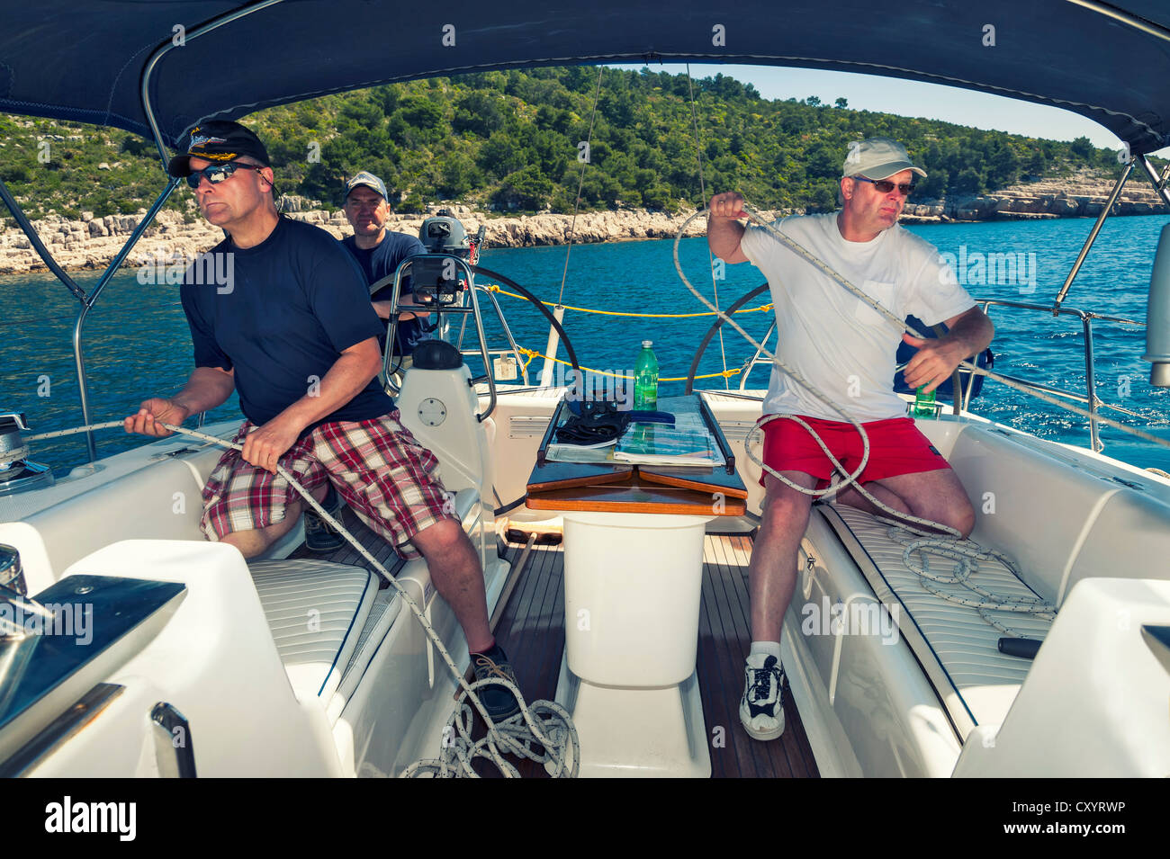 Trois hommes d'équipage d'un bateau à voile à l'arrière d'un yacht durant une manœuvre de voile au large de la côte croate, Croatie, Europe Banque D'Images