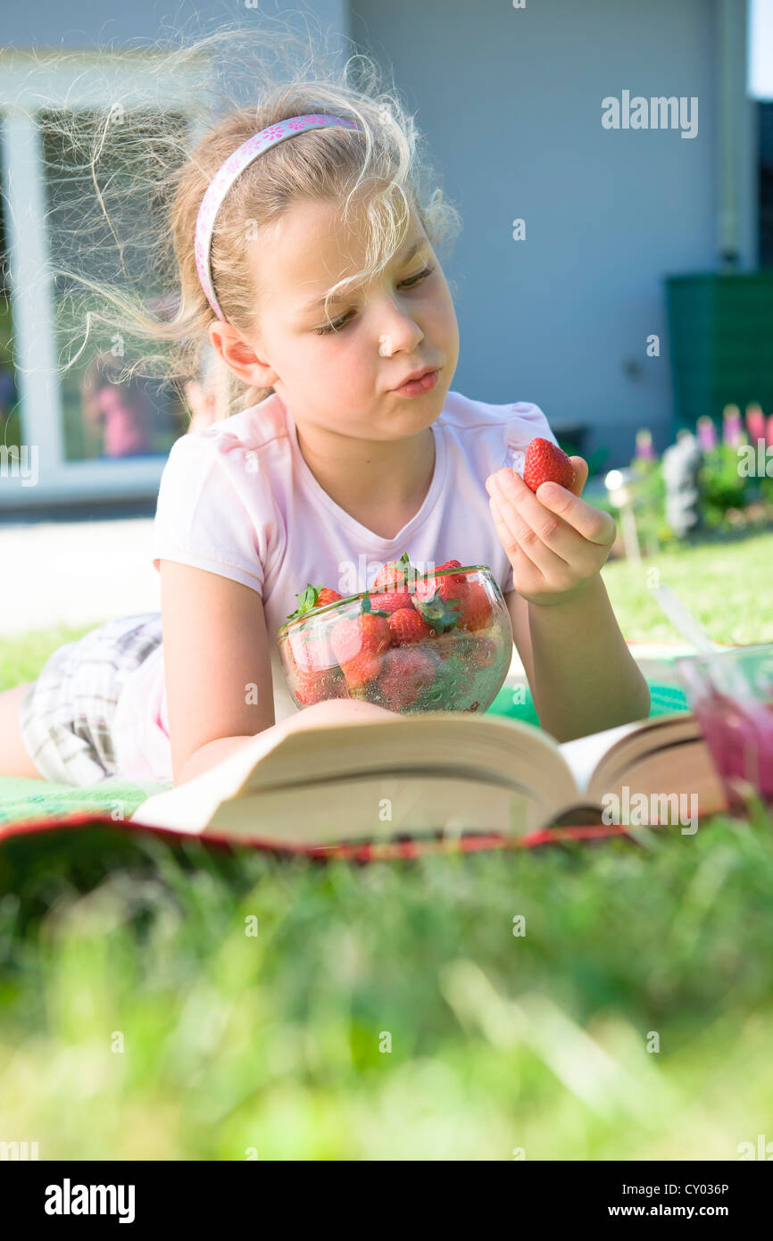 Fille avec des fraises et un livre dans le jardin Banque D'Images