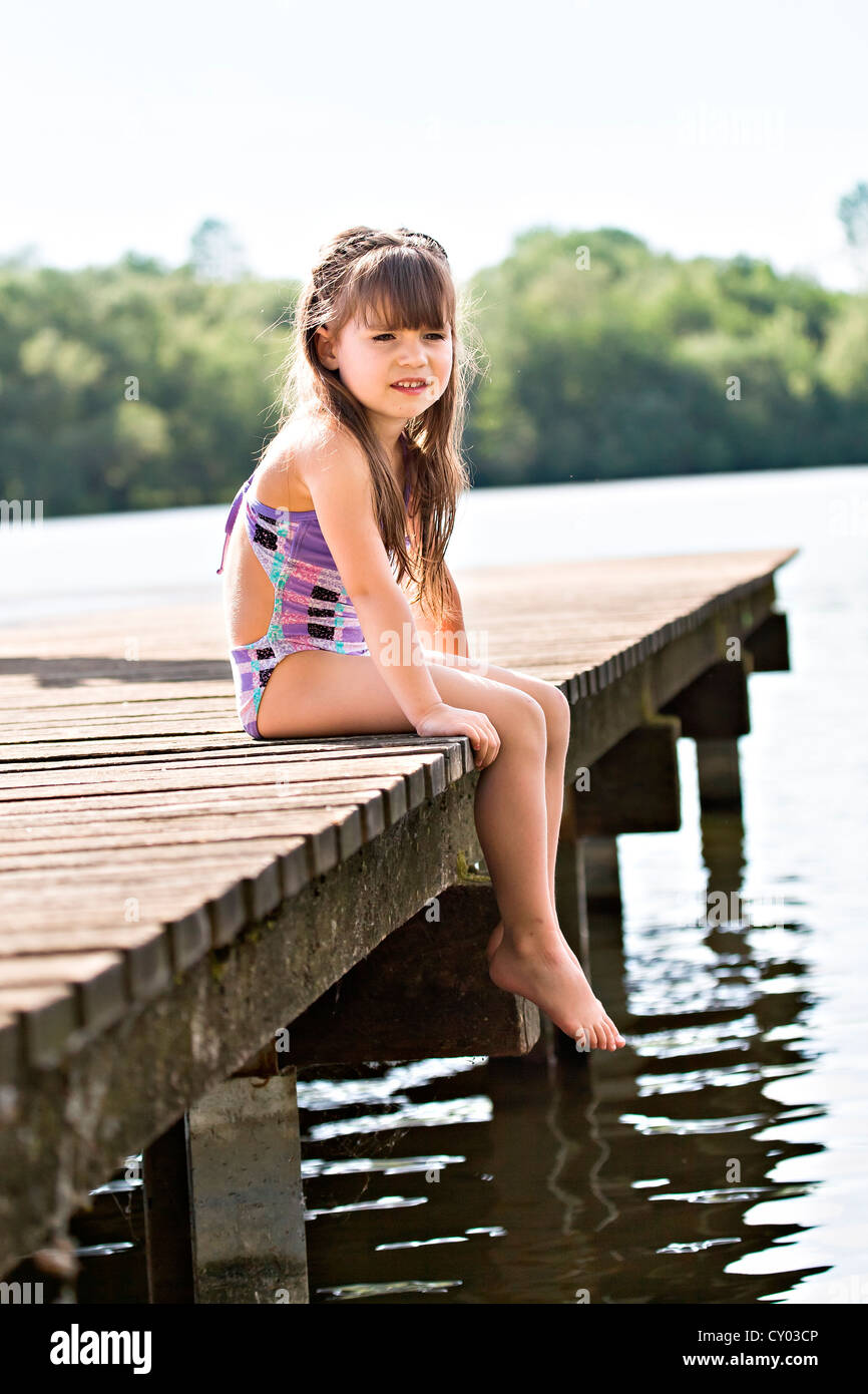 Girl sitting on jetty at lakeside Banque D'Images