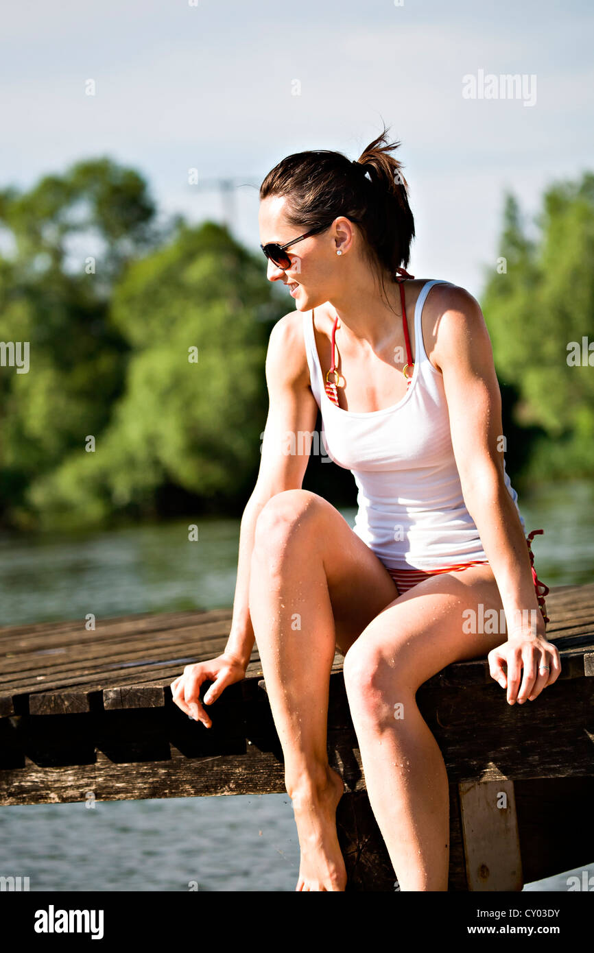 Young woman sitting on jetty at lakeside Banque D'Images