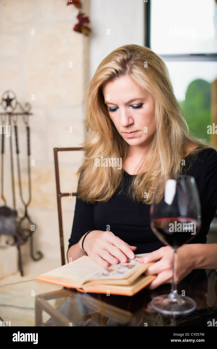 Femme de race blanche dans la trentaine de lire un livre tout en buvant un verre de vin rouge Banque D'Images