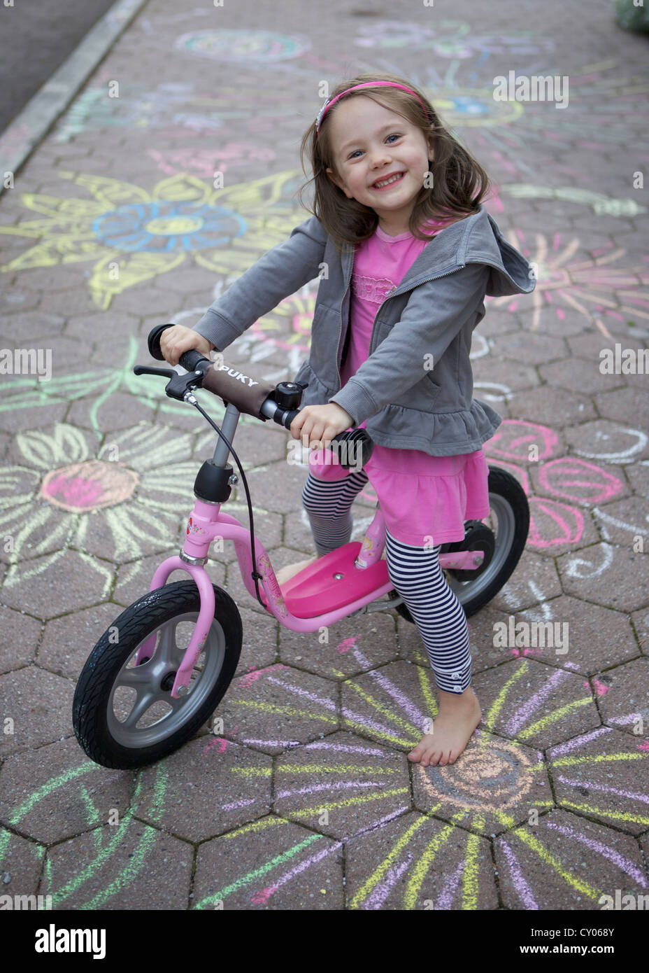 Fillette de trois ans assis sur un vélo, marche sur une rue peint avec de la craie, Rosenheim, Bavière Banque D'Images