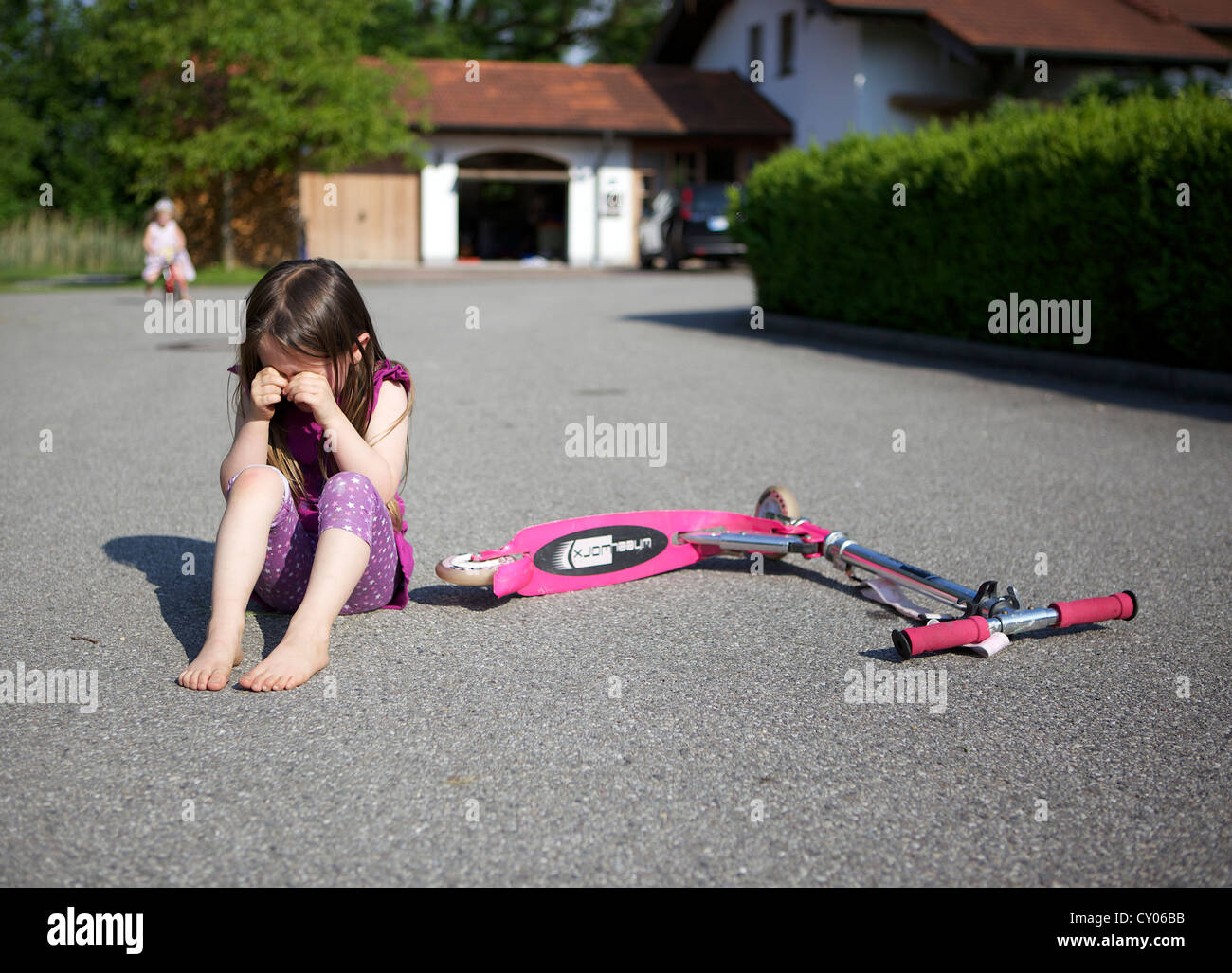 Petite fille, trois ans, est parti de son triporteur, assis sur le plancher en pleurant Banque D'Images