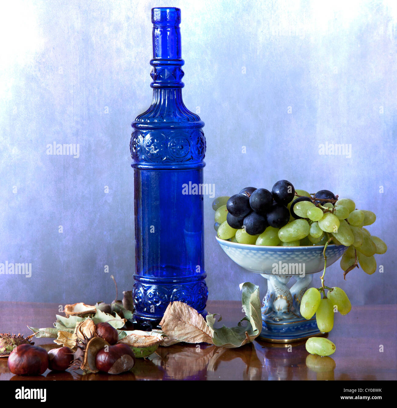 Still Life : Flacon en verre bleu avec des fruits d'automne, les raisins et châtaignes, et les feuilles sur une table polie en bois Banque D'Images