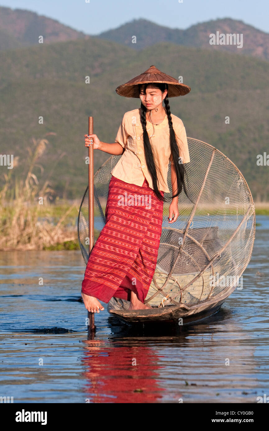 Le Myanmar, Birmanie. Jeune femme birmane l'Aviron avec une jambe, à la recherche d'un endroit pour mettre son filet de pêche. Lac Inle, l'État Shan. Banque D'Images