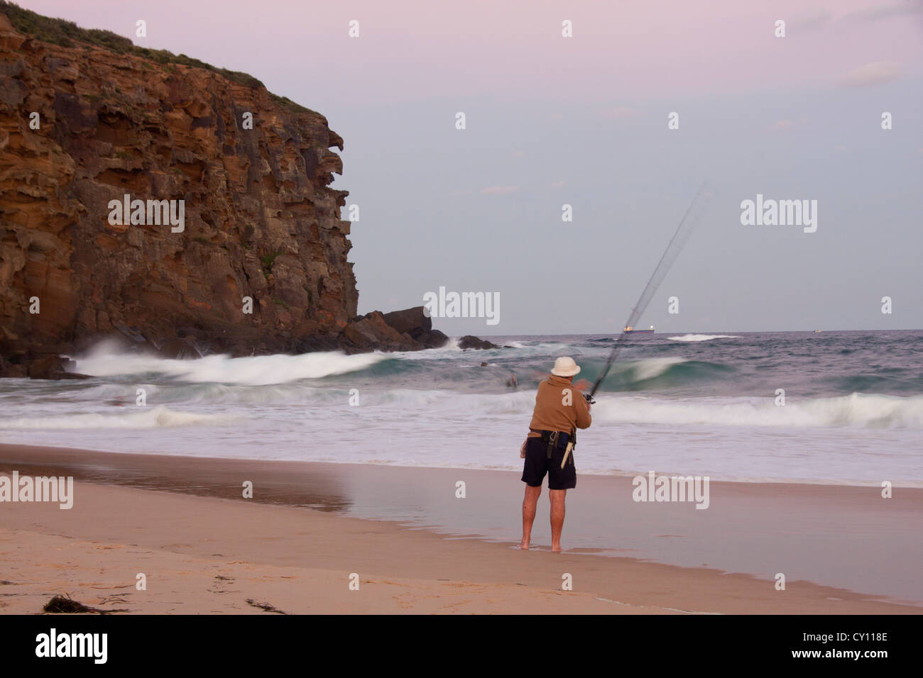 L'homme pêche en mer à la tombée de la falaise à Rousse Plage avec en arrière-plan Newcastle Australie Nouvelle Galles du Sud Banque D'Images