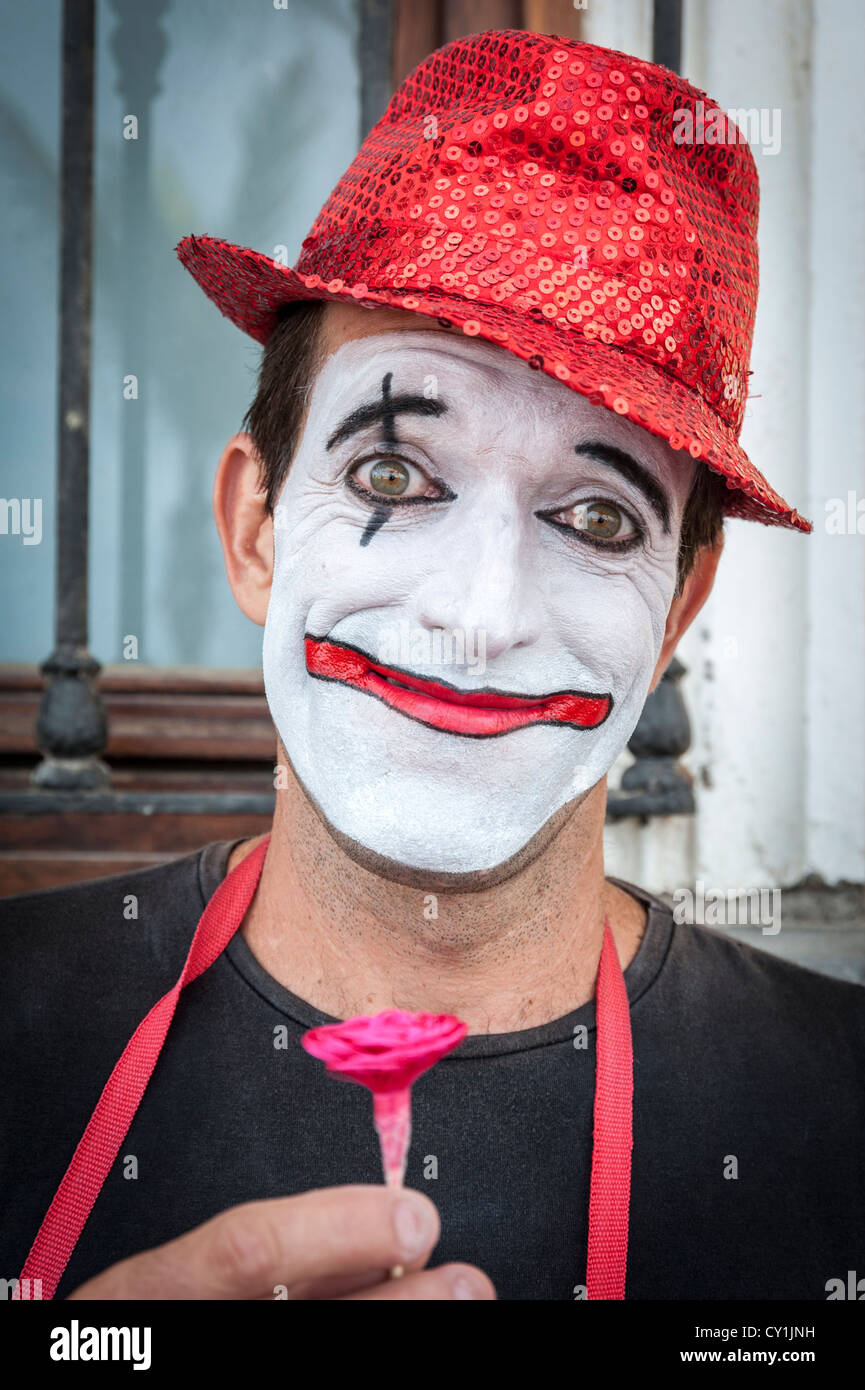 Un portrait d'un artiste de rue clown à Las Palmas de Gran Canaria Espagne portant un chapeau avec un visage blanc, tenant une fleur Banque D'Images