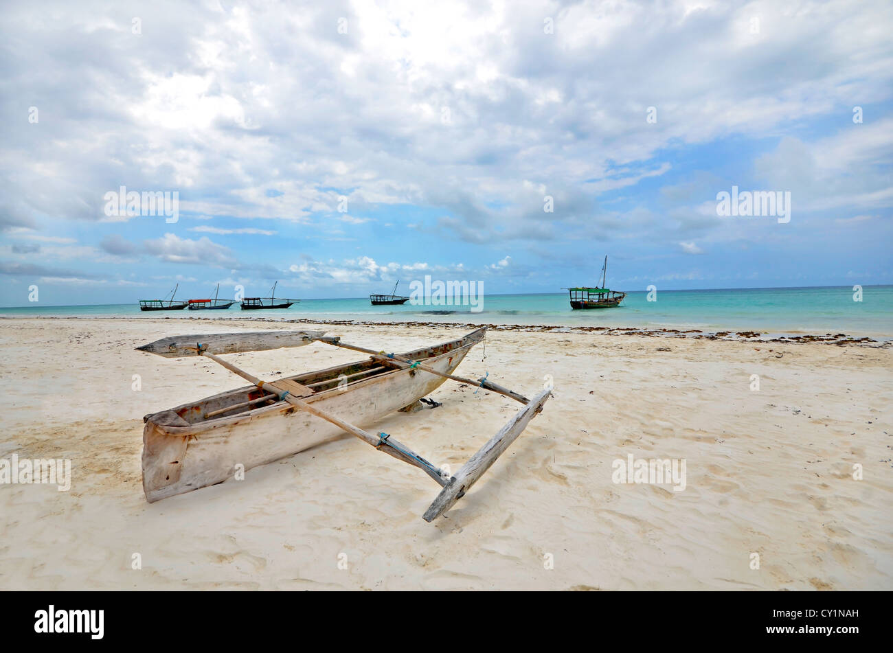 Bateau de pêche en bois sur une plage de l'île de Zanzibar avec bateaux de touristes dans l'arrière-plan sur une journée ensoleillée. Banque D'Images