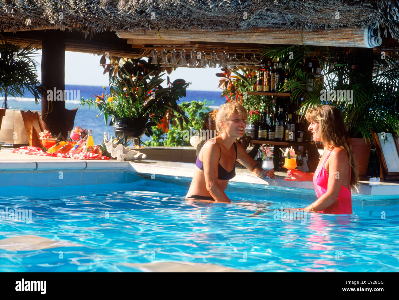 Deux femmes touristes siroter des boissons tropicales en piscine avec bar à La Digue Island Lodge aux Seychelles sous un ciel ensoleillé Banque D'Images