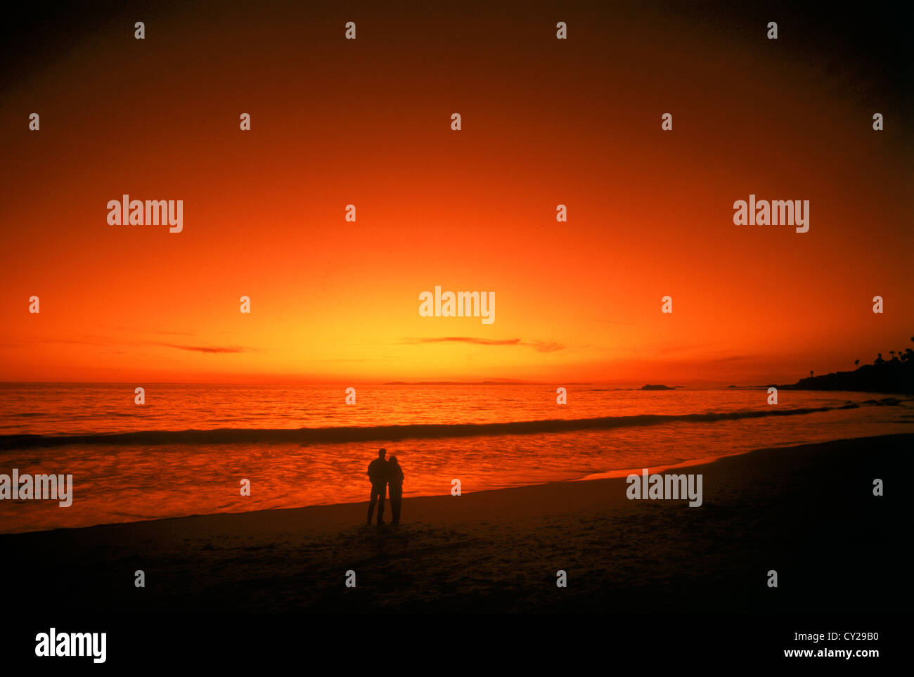 Couple standing on sandy shore avec peinture coucher de l'océan Pacifique et du ciel Banque D'Images