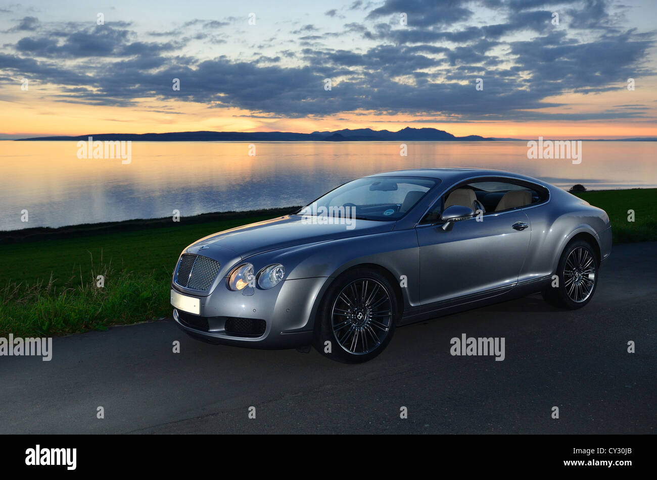 Bentley Continental GT à côté de la plage et de la mer au coucher du soleil et des îles dans l'arrière-plan et nuages dans le ciel Banque D'Images