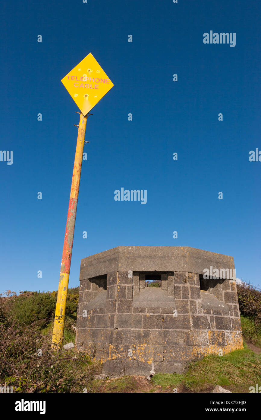 Un panneau jaune indiquant le câble téléphonique à côté d'un temps de guerre sur les falaises au-dessus de la défense Porthcurno, Cornwall, United Kingdom Banque D'Images