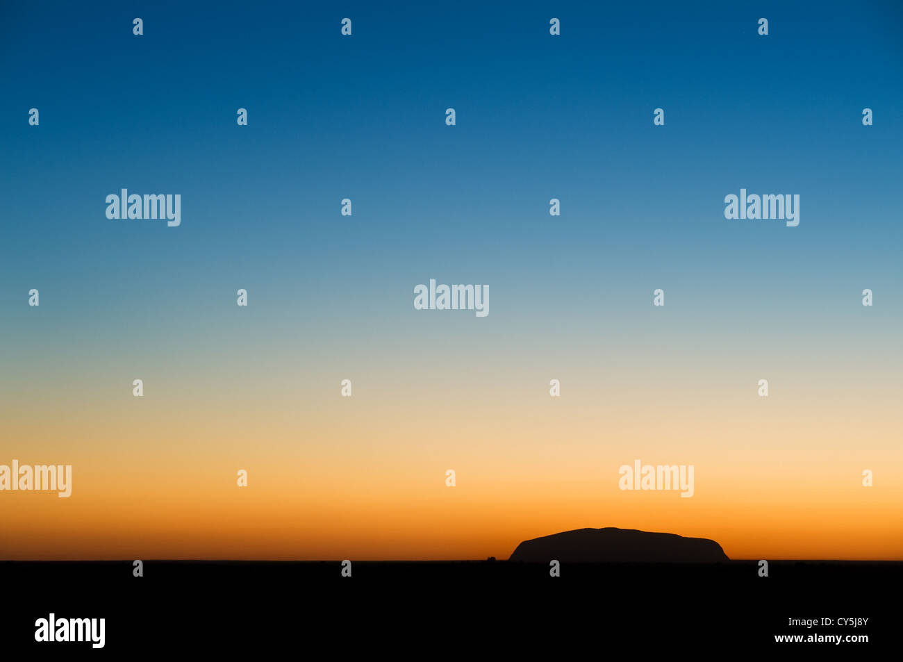 Silhouette noire d'Uluru en face d'un horizon ensoleillé. Banque D'Images