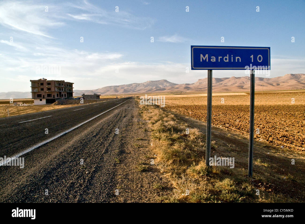 Un panneau routier et une route allant vers le nord à travers la plaine syrienne en direction de la ville de Mardin, dans la région orientale de l'Anatolie, au sud-est de la Turquie. Banque D'Images