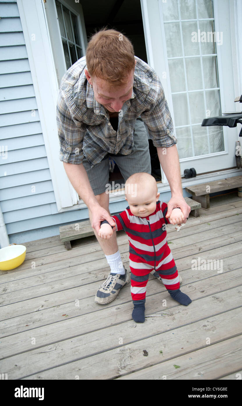 Un bébé apprend à marcher avec son père tenant ses mains Banque D'Images