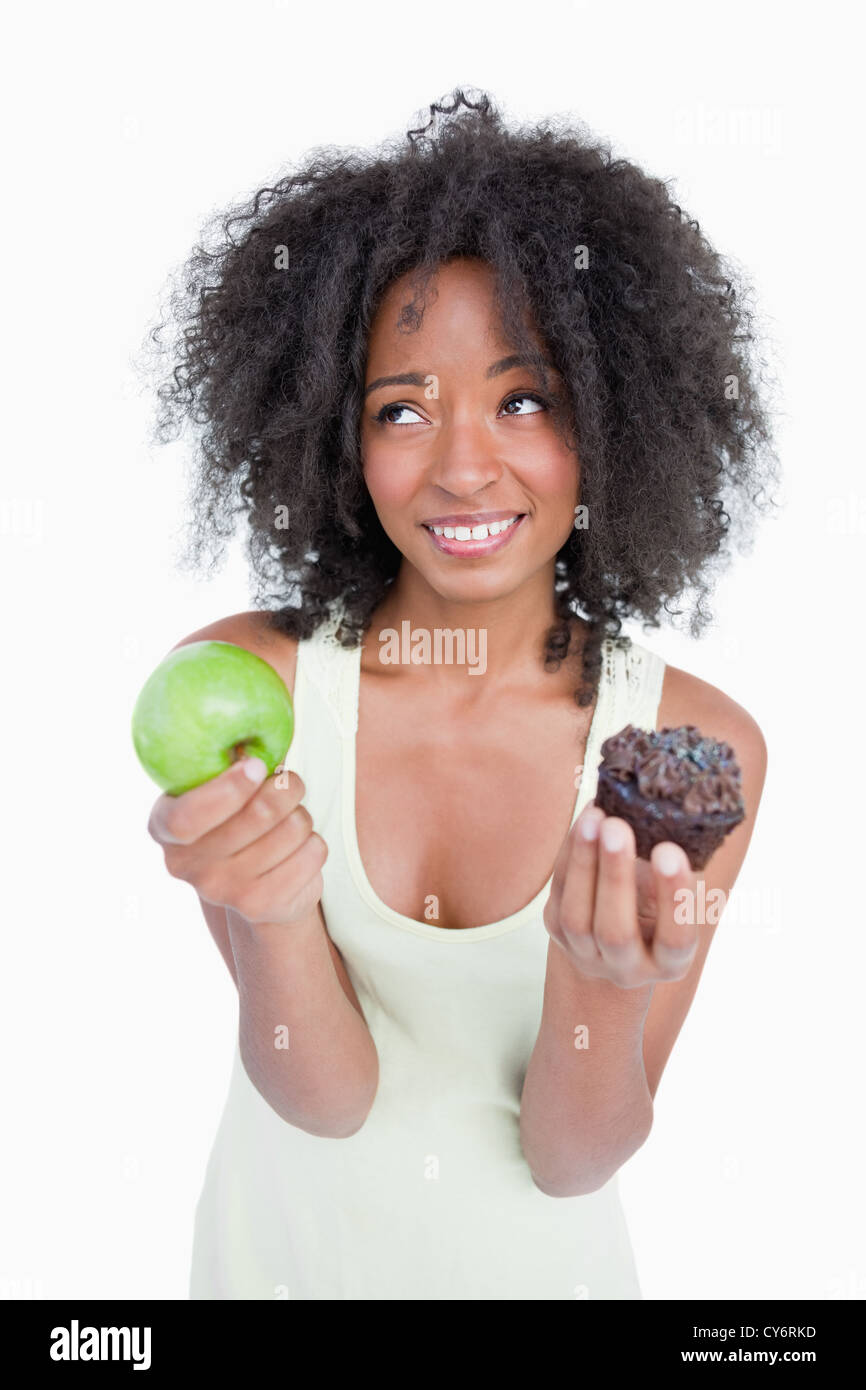Jeune femme à la recherche jusqu'à demander de l'aide pour choisir entre un fruit et chocolat Banque D'Images