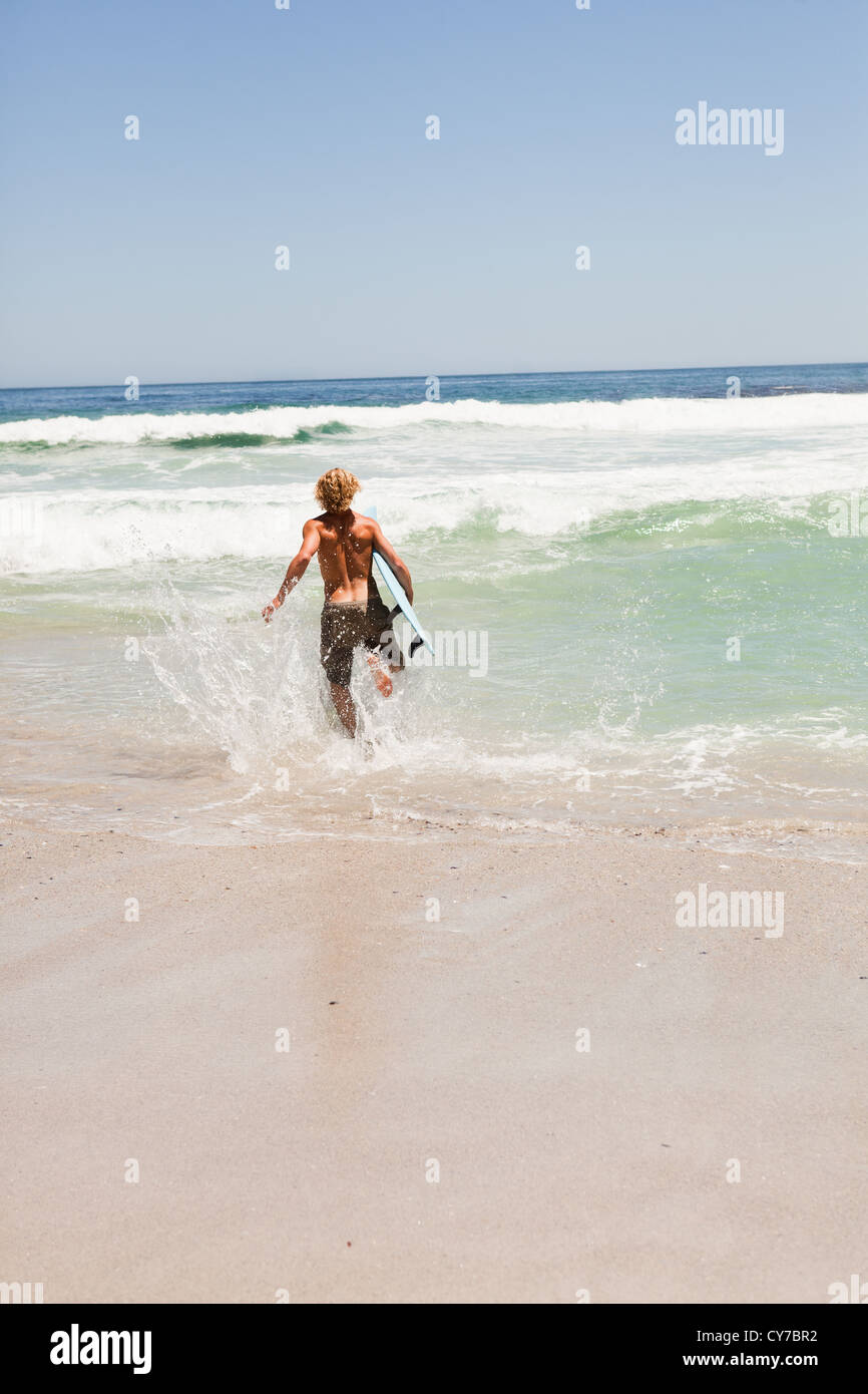 Jeune homme qui court dans l'eau avec son surf Banque D'Images