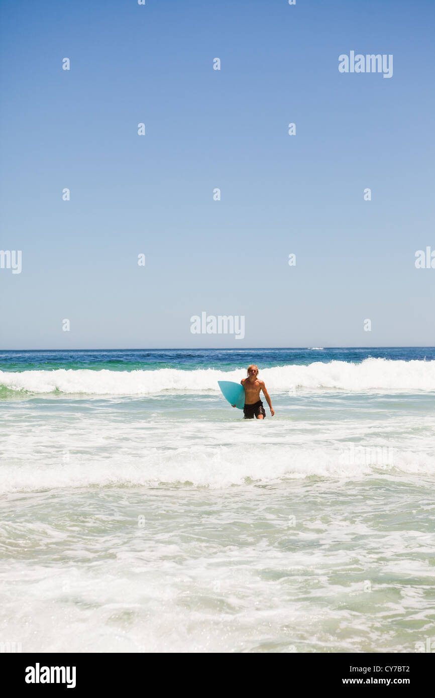 Jeune homme marchant dans l'eau avec son surf Banque D'Images