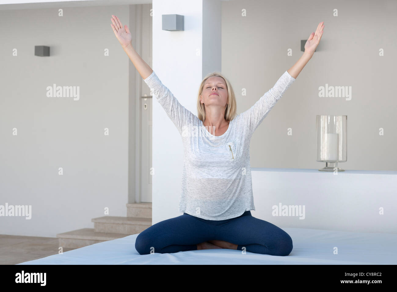 Young woman exercising on bed with arms raised Banque D'Images