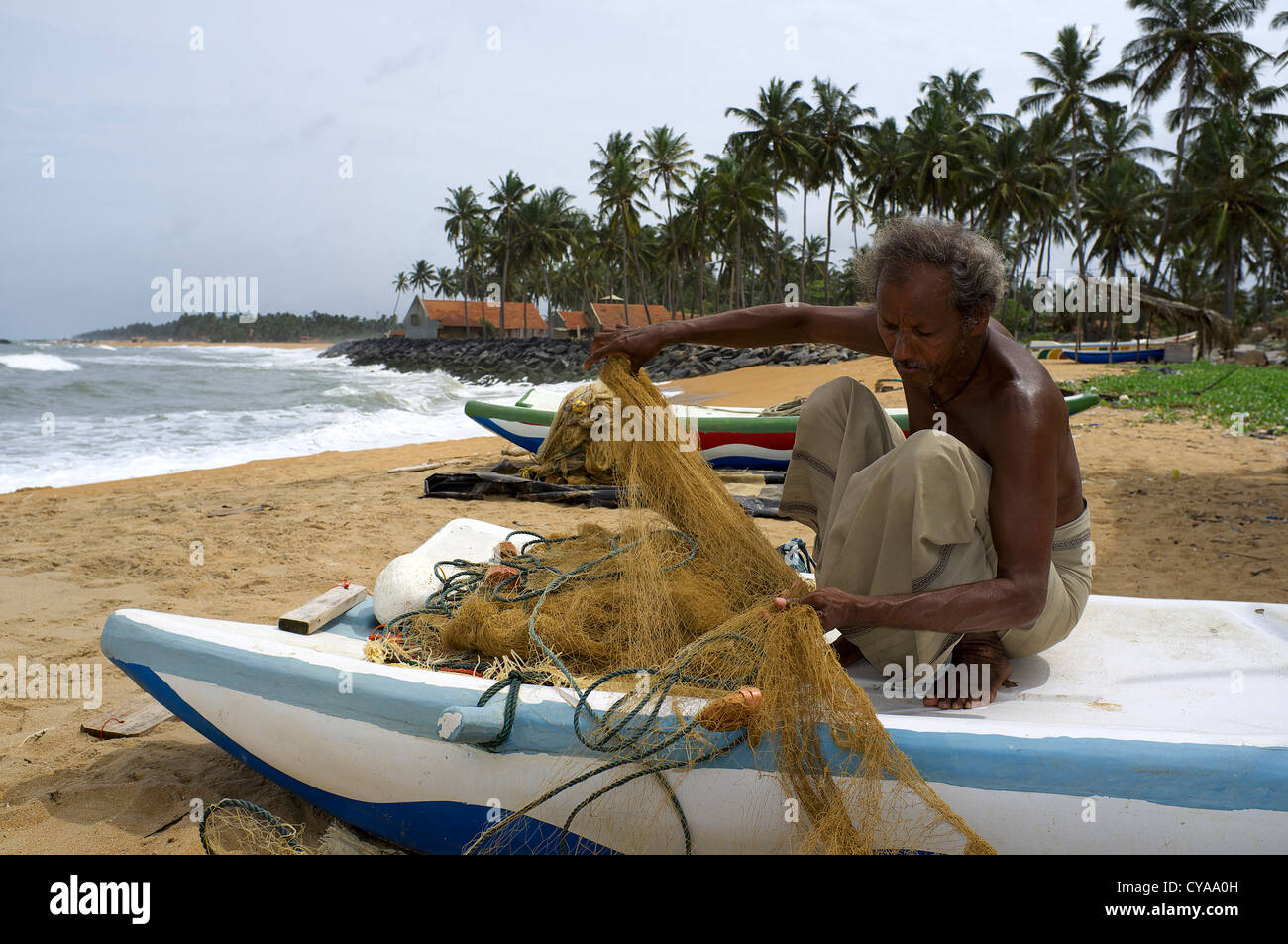 Sri Lanka pêcheur réparant son filet de pêche tout en étant assis sur son petit bateau, Waikkal, Sri Lanka Banque D'Images