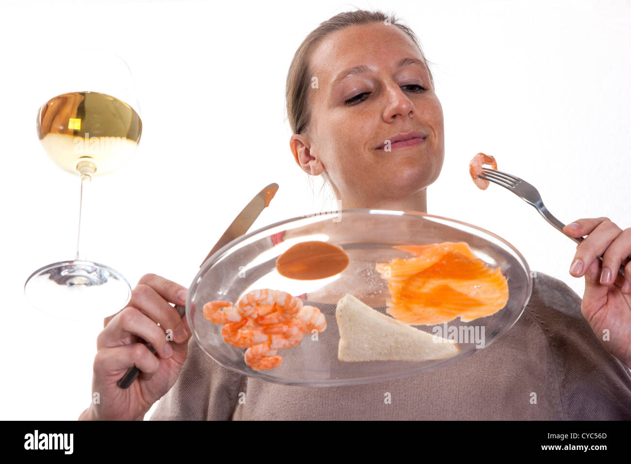 Jeune femme est en train de manger à une table en verre. Un saumon fumé crevettes avec un verre de vin blanc, de pain grillé et un cocktail vinaigrette. Banque D'Images