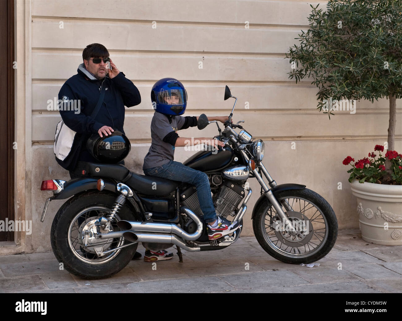 Un jeune garçon portant un casque d'accident à cheval sur la moto de son père, à Syracuse (Syracuse), en Sicile, en Italie Banque D'Images