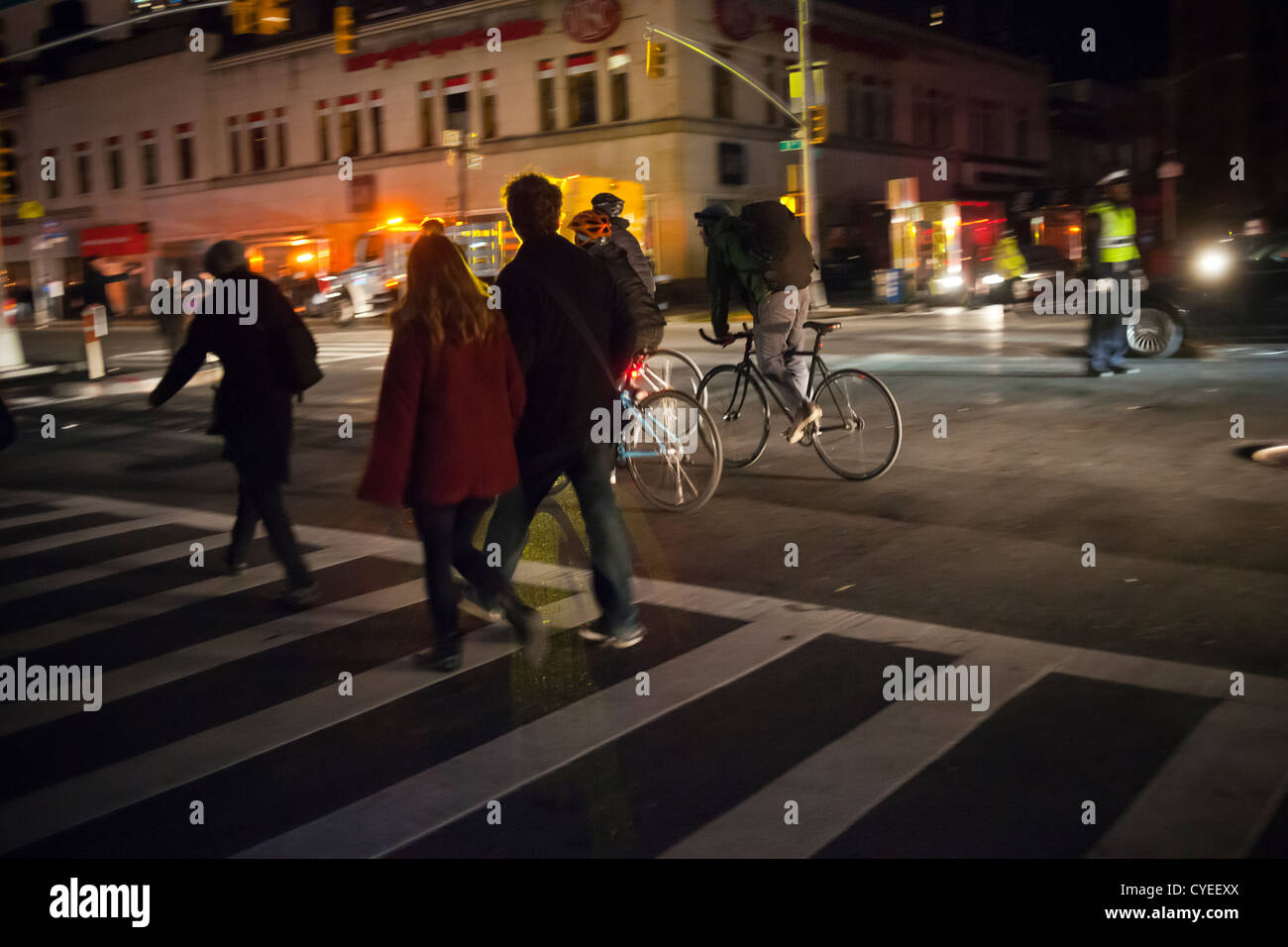 Comme la nuit tombe, les New-Yorkais traverser une intersection à Chelsea à New York par la lumière des phares d'automobile Banque D'Images