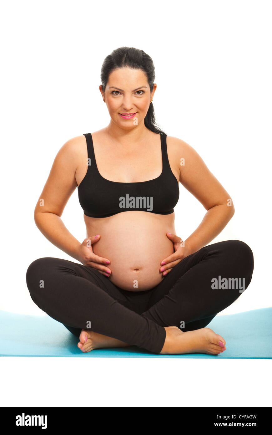 Happy pregnant woman standing on fitness tapis bleu et de toucher son ventre contre fond blanc Banque D'Images