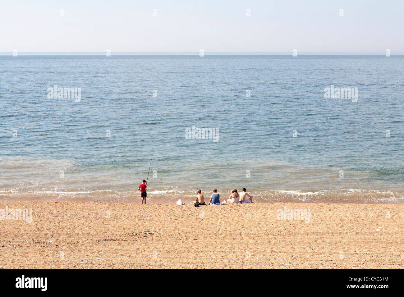 Groupe de jeunes gens assis sur UK beach avec l'un tenant une canne à pêche Banque D'Images