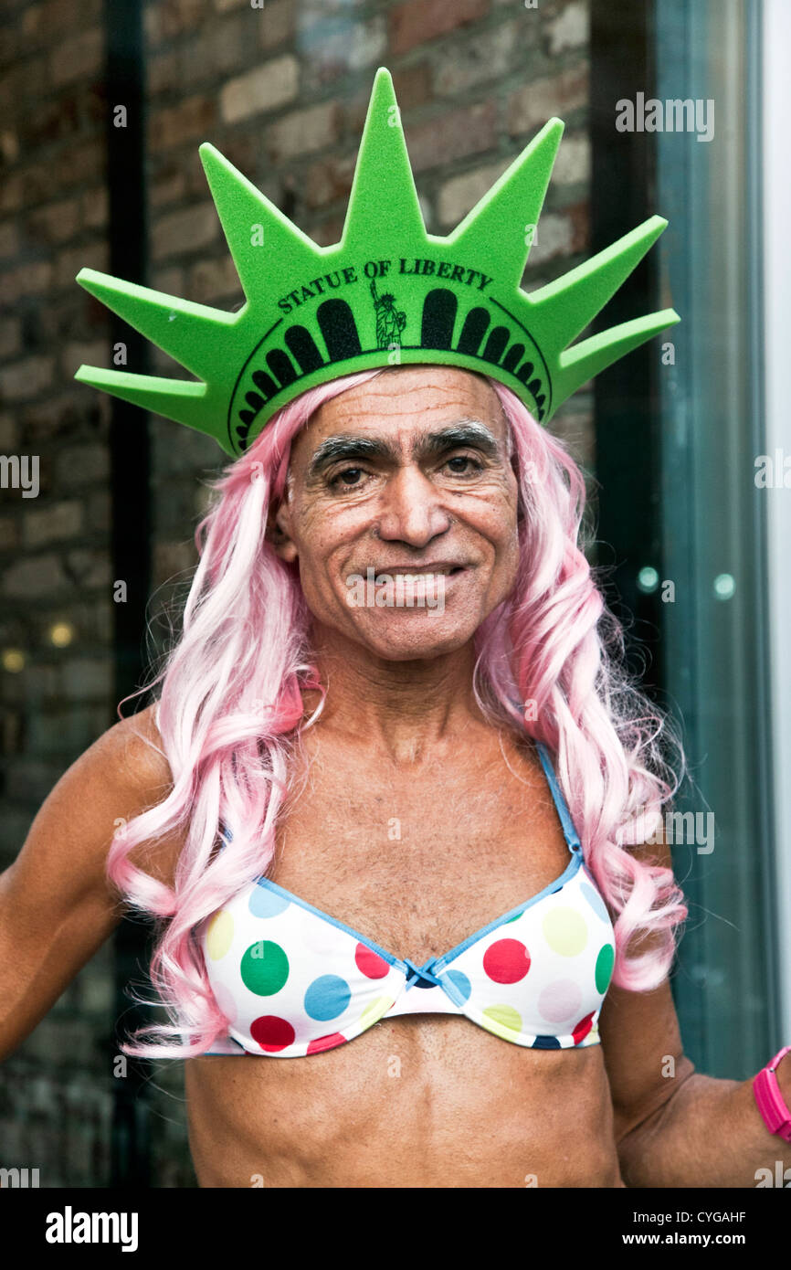 Tannés smiling middle aged homme travesti habillé pour l'Halloween en bikini à pois perruque rose & Statue de la liberté de la couronne à pointes Banque D'Images