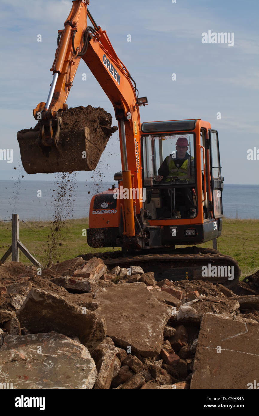 Excavatrice Digger voie dépose hardcore de butin falaise la démolition du site. Littoral Happisburgh, Norfolk. Banque D'Images