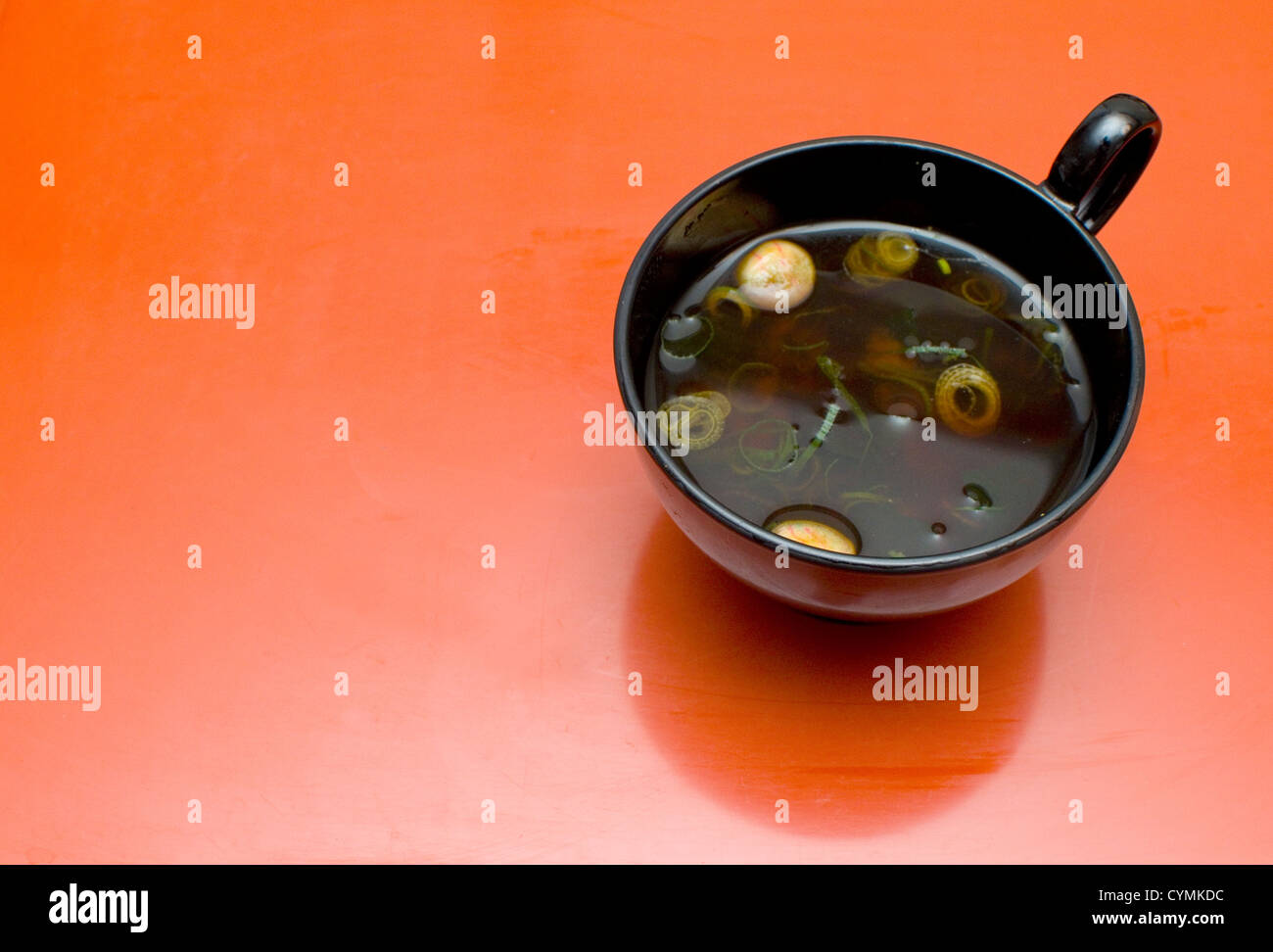 La soupe miso dans un bol de laque noire sur un fond rouge / orange. Banque D'Images