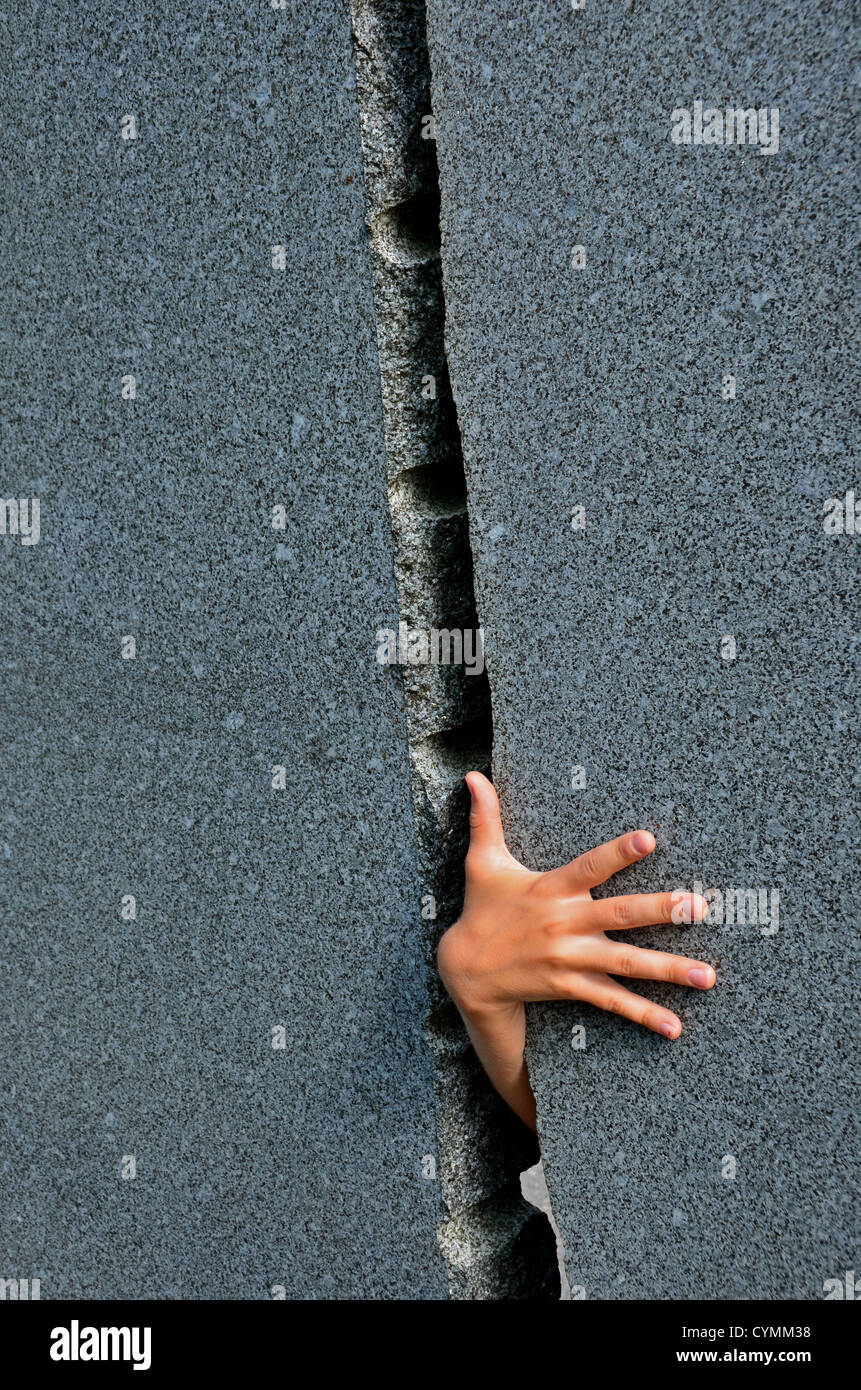 Main d'UN enfant saisit à travers l'écart étroit dans le mur de marbre Banque D'Images