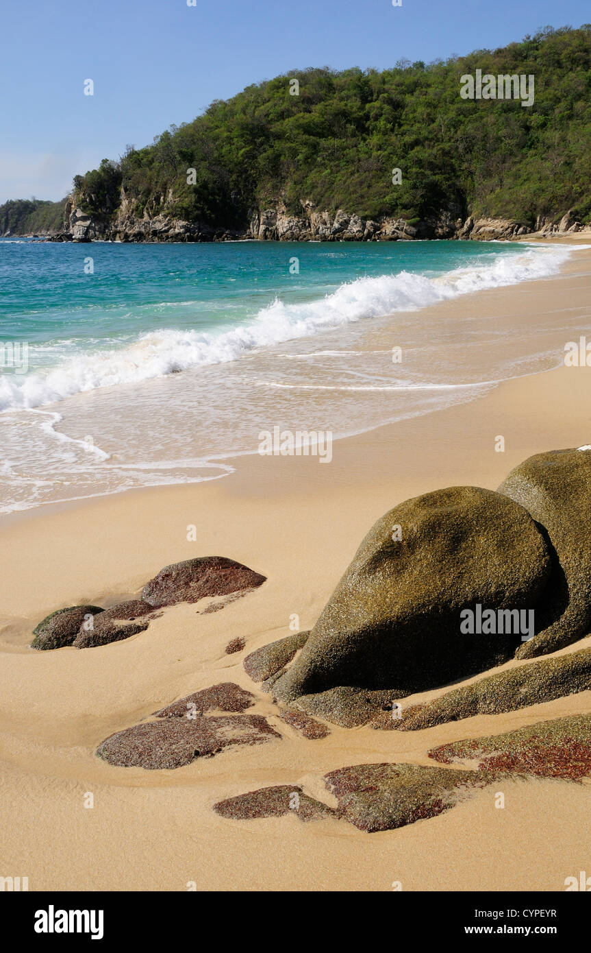 Mexique, Oaxaca, Huatulco, Bahia Chahue, rochers et plage de sable déserte, avec surf sur la rive et promontoire rocheux au-delà. Banque D'Images