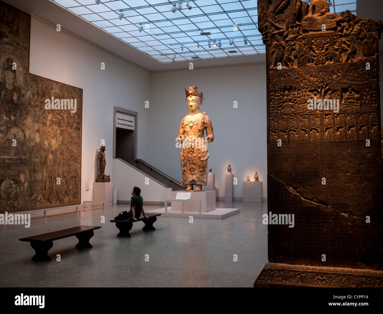 Exposition d'antiquités du Metropolitan Museum of Art New York City | NEW YORK, États-Unis — Un visiteur contemple des antiquités dans l'une des nombreuses expositions du Metropolitan Museum of Art. La galerie présente une grande statue debout, une stèle sculptée et une fresque murale, probablement faisant partie de la collection des Arts de l'Asie du Sud et du Sud-Est. L'exposition met en lumière le riche héritage culturel de la région. Banque D'Images