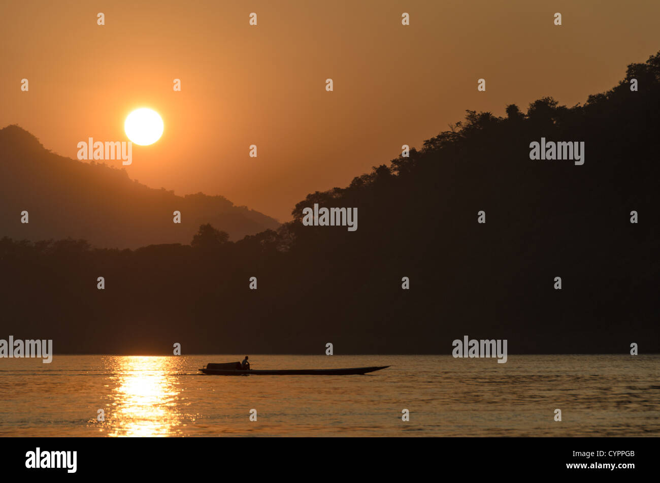 LUANG PRABANG, Laos - un sampan motorisés traverse la rivière juste avant que le soleil se couche derrière les moutnains sur le Mékong près de Luang Prabang, Laos. Banque D'Images