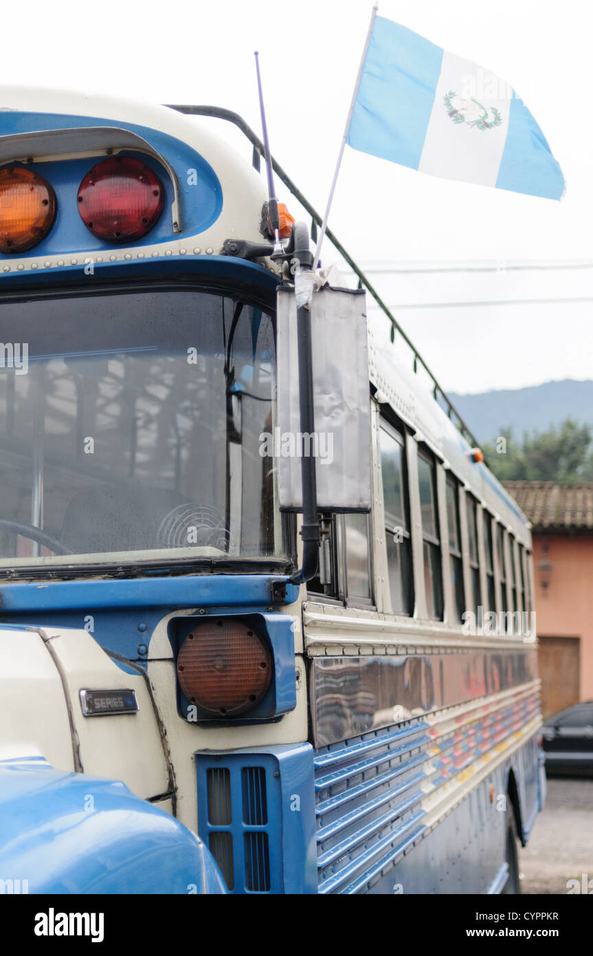 Bus de poulet drapeau guatémaltèque Antigua Guatemala // ANTIGUA GUATEMALA, Guatemala — Un bus de poulet bleu et blanc avec drapeau guatémaltèque derrière le Mercado Municipal (marché de la ville) à Antigua, Guatemala. De ce vaste échangeur de bus central, les itinéraires rayonnent à travers le Guatemala. Souvent peints de couleurs vives, les bus de poulet sont des bus scolaires américains modernisés et fournissent un mode de transport bon marché dans tout le pays. Banque D'Images